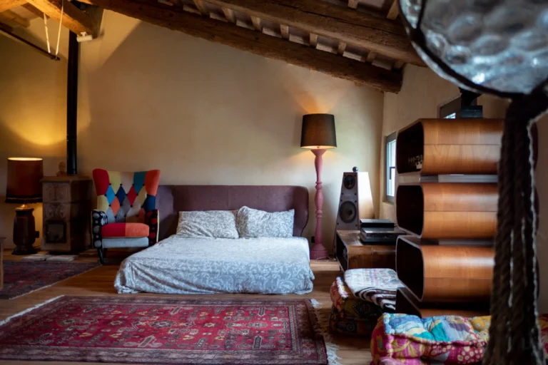 Camera in mansarda con letto matrimoniale, stufa in maiolica e poltrona a rombi colorati