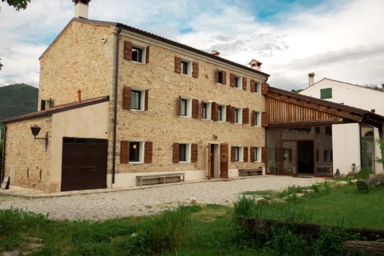 Facciata in pietra del casale Tana del Tasso con corte in ghiaia e veranda vetrata