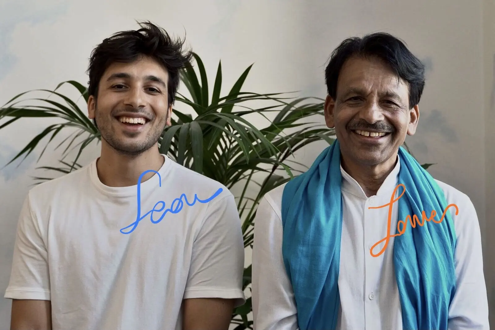 Sean e James Eruppakkattu, padre e figlio nonché maestri della Scuola Yoga Shanti, sono seduti mentre sorridono, con le loro firme sovrimpresse, di colore azzurro ed arancione
